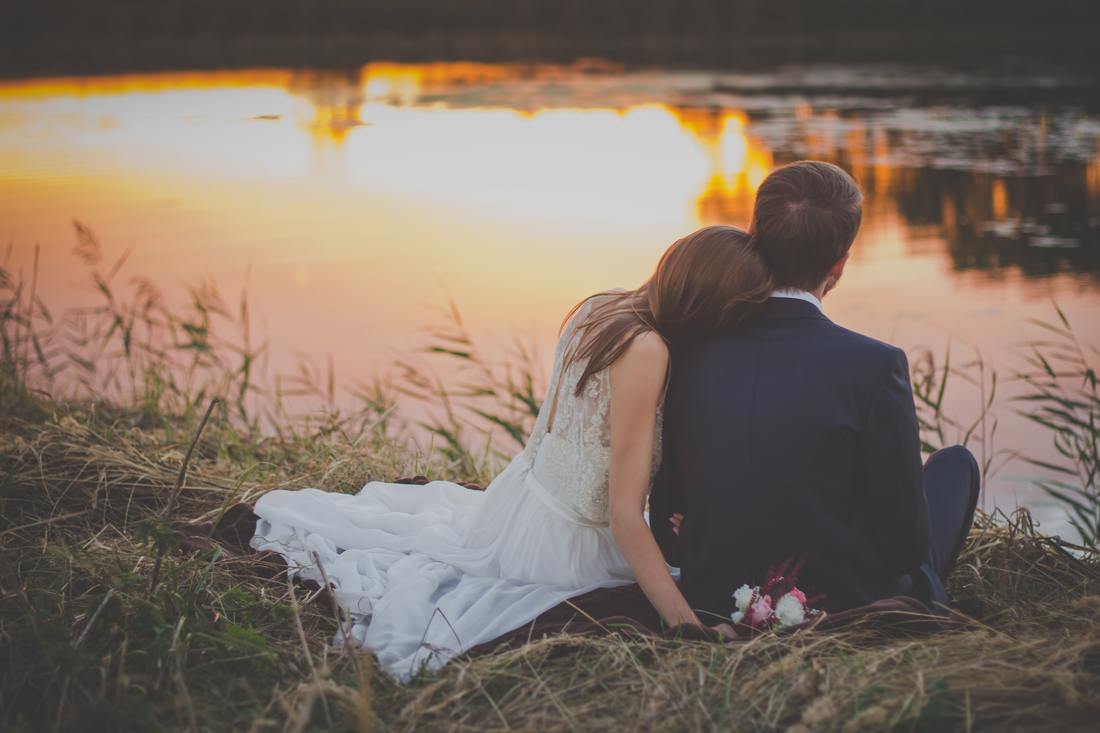 wedding couple sitting on grass by water